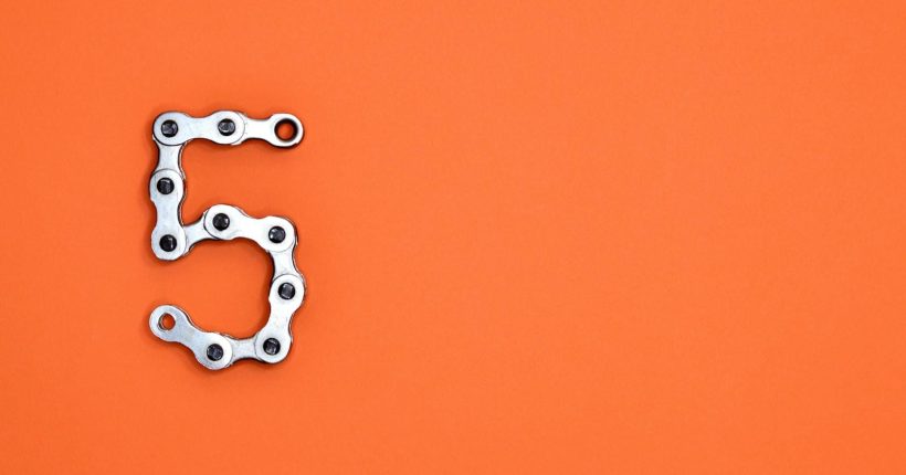 Photo by Miguel Á. Padriñán Creative arrangement of a chrome bicycle chain forming the number 5 on a vibrant orange background.
