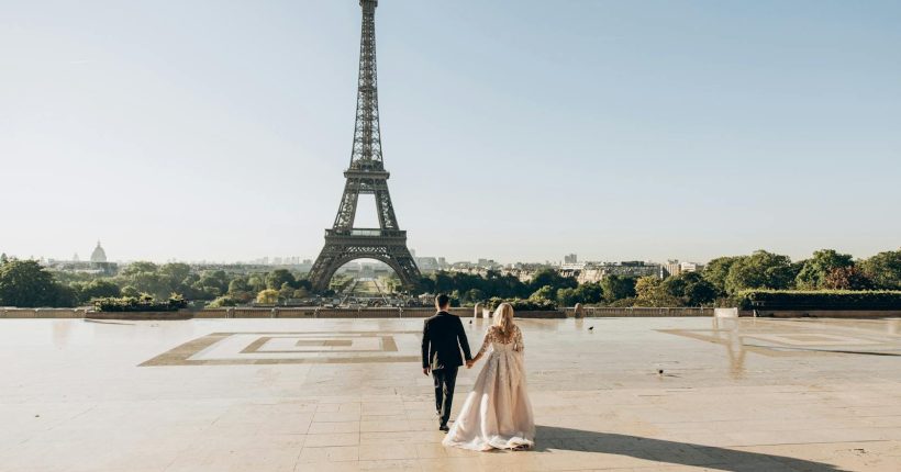 Photo by Dimitri Kuliuk A bride and groom sharing a romantic moment in front of the iconic Eiffel Tower in Paris.